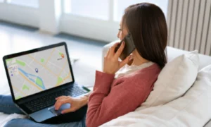 Mujer consultando un mapa local en su portátil mientras realiza una llamada telefónica para contactar con una inmobiliaria.